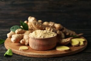 Board with ginger and ginger powder on wooden background